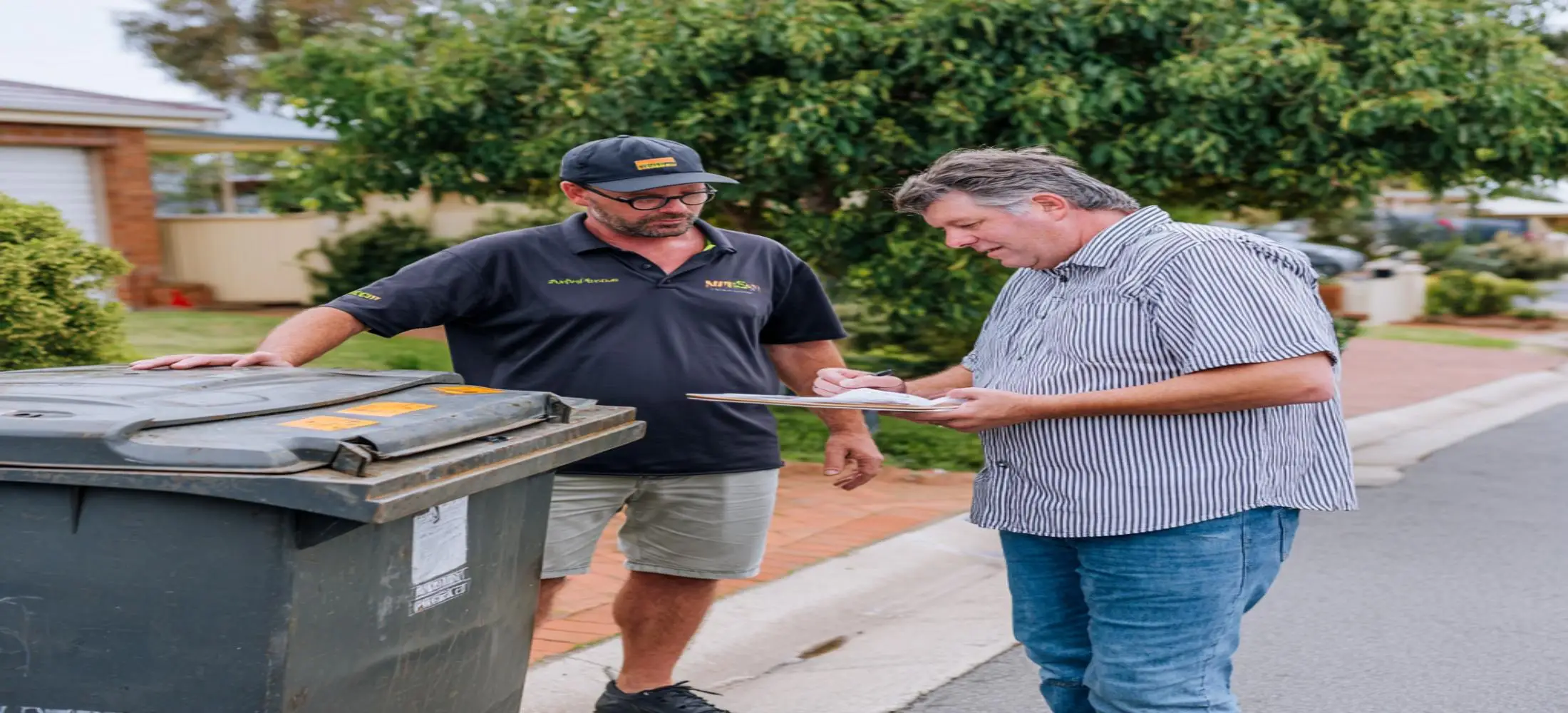 Homeowner discussing waste disposal needs beside a skip bin while comparing cheap skip bin hire Bunbury options