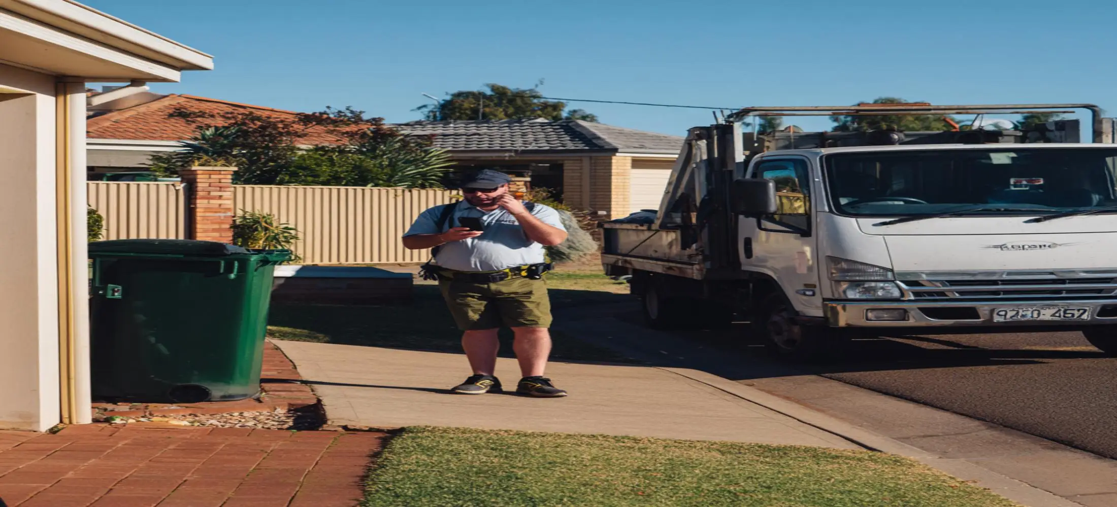 Homeowner discussing waste disposal requirements by phone while comparing cheapest skip bin Bunbury options