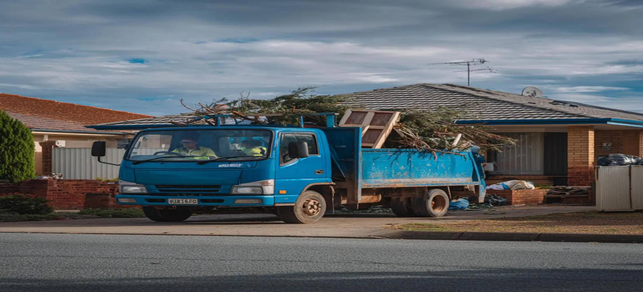 Blue rubbish removal truck collecting furniture, garden waste and mixed rubbish during a rubbish removal Bunbury property cleanup project